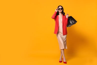 Beautiful young woman with paper shopping bags on yellow background. Space for text