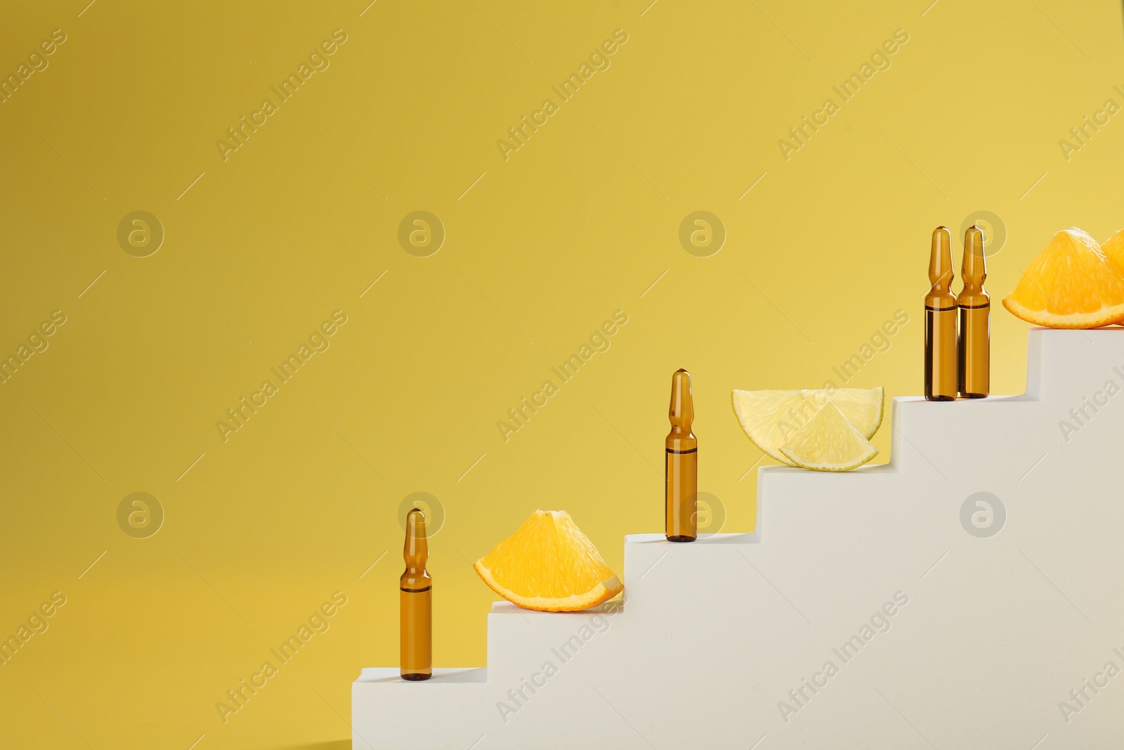 Photo of Stylish presentation of skincare ampoules with vitamin C and citrus slices on decorative stairs against yellow background, closeup. Space for text