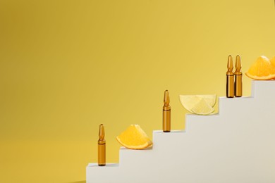 Photo of Stylish presentation of skincare ampoules with vitamin C and citrus slices on decorative stairs against yellow background, closeup. Space for text