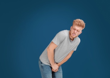 Photo of Young man suffering from pain on blue background, space for text. Urology problems