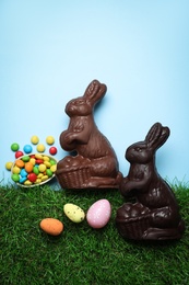 Photo of Chocolate Easter bunnies, eggs and candies with green grass on light blue background