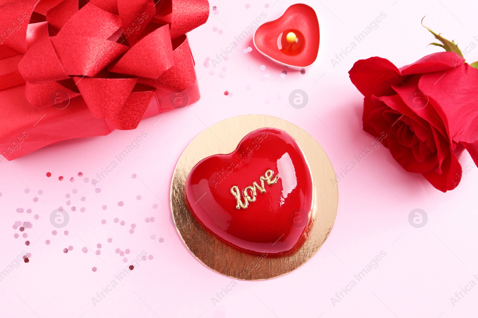 Photo of St. Valentine's Day. Delicious heart shaped cake, gift and rose on light pink background, flat lay