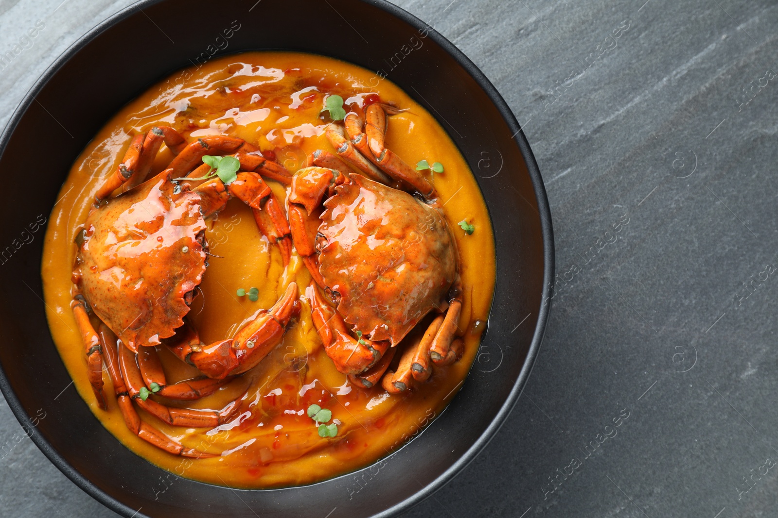 Photo of Delicious boiled crabs with sauce in bowl on grey textured table, top view. Space for text