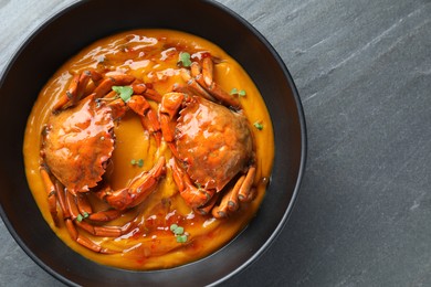 Delicious boiled crabs with sauce in bowl on grey textured table, top view. Space for text