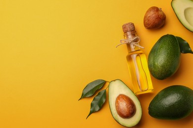 Photo of Glass bottle of cooking oil and fresh avocados on yellow background, flat lay. Space for text