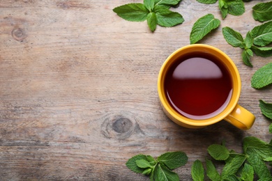 Cup with hot aromatic mint tea and fresh leaves on wooden table, flat lay. Space for text