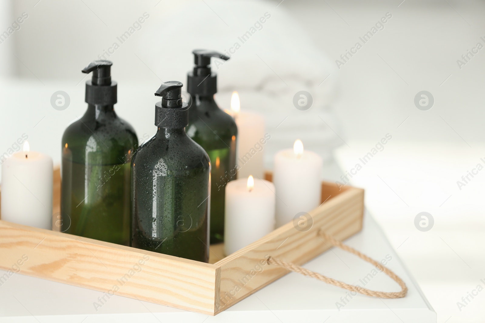 Photo of Wooden tray with soap dispensers and burning candles on white table. Space for text