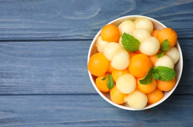 Melon balls and mint in bowl on blue wooden table, top view. Space for text