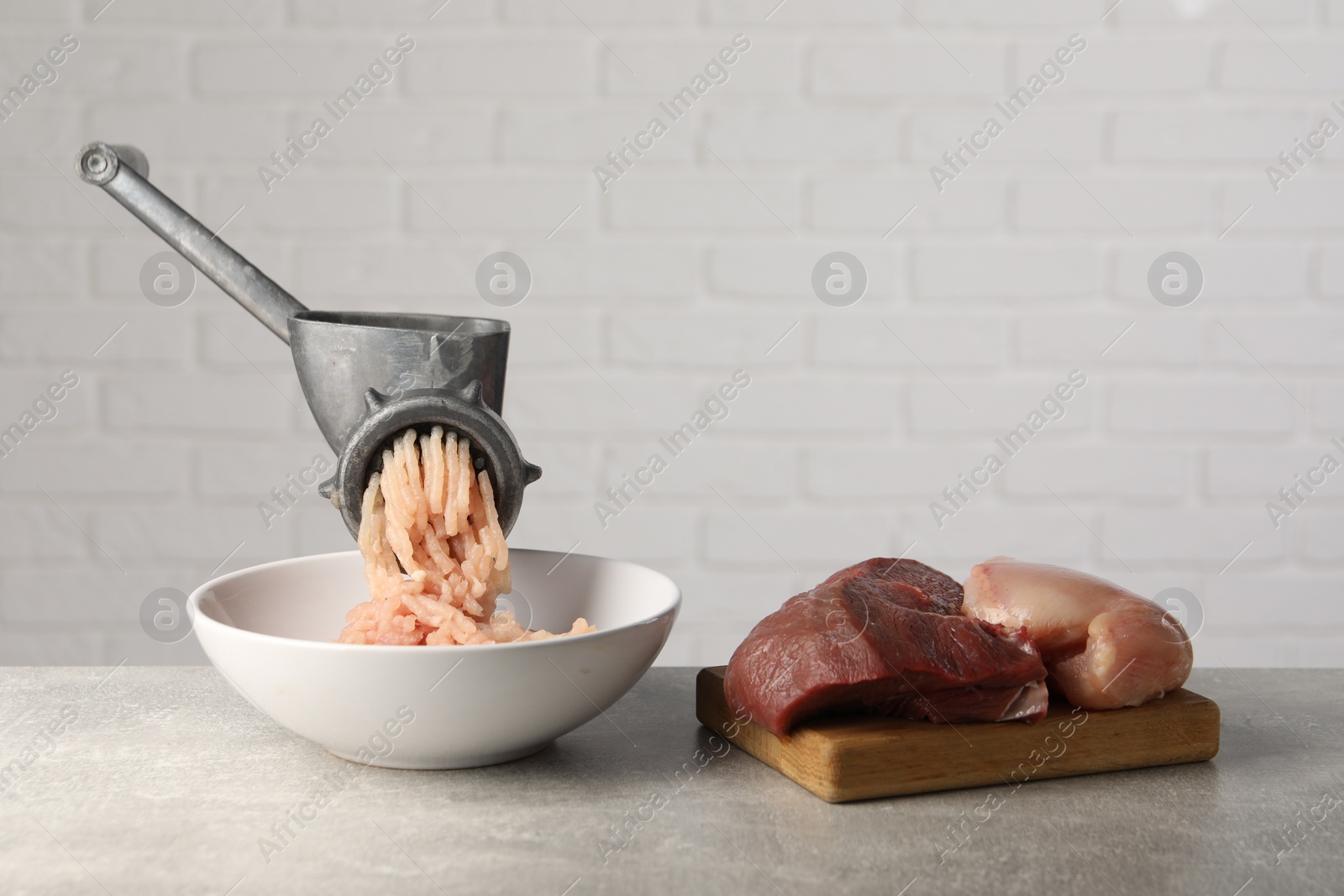 Photo of Metal meat grinder with mince, raw chicken and beef on grey table near light wall