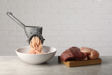 Metal meat grinder with mince, raw chicken and beef on grey table near light wall