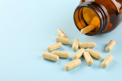 Photo of Bottle and vitamin capsules on light blue background, closeup. Space for text