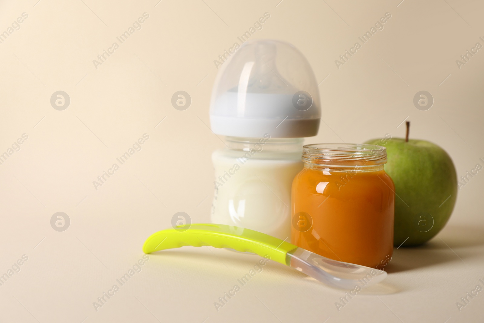 Photo of Healthy baby food in jar, bottle of milk, apple and spoon on beige background. Space for text