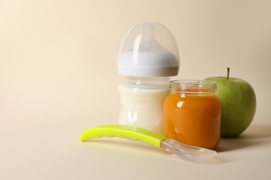 Photo of Healthy baby food in jar, bottle of milk, apple and spoon on beige background. Space for text