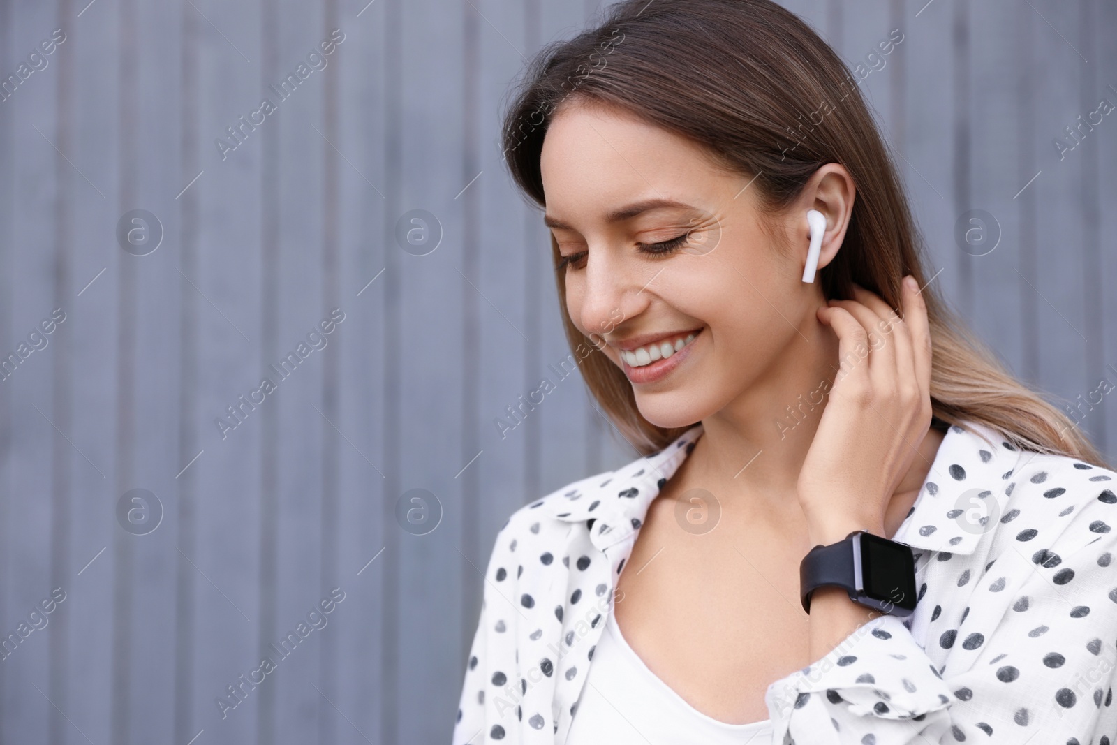 Photo of Young woman with wireless headphones listening to music near grey wall. Space for text