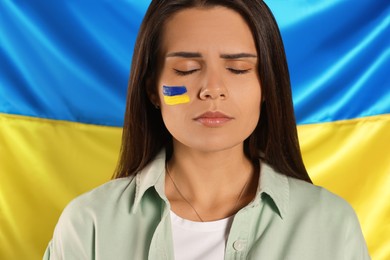 Photo of Sad young woman with face paint near Ukrainian flag