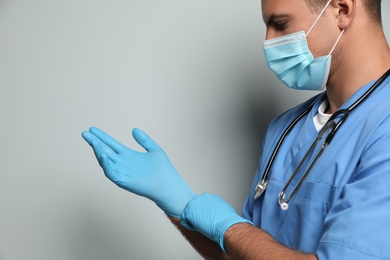 Photo of Doctor in protective mask putting on medical gloves against light grey background