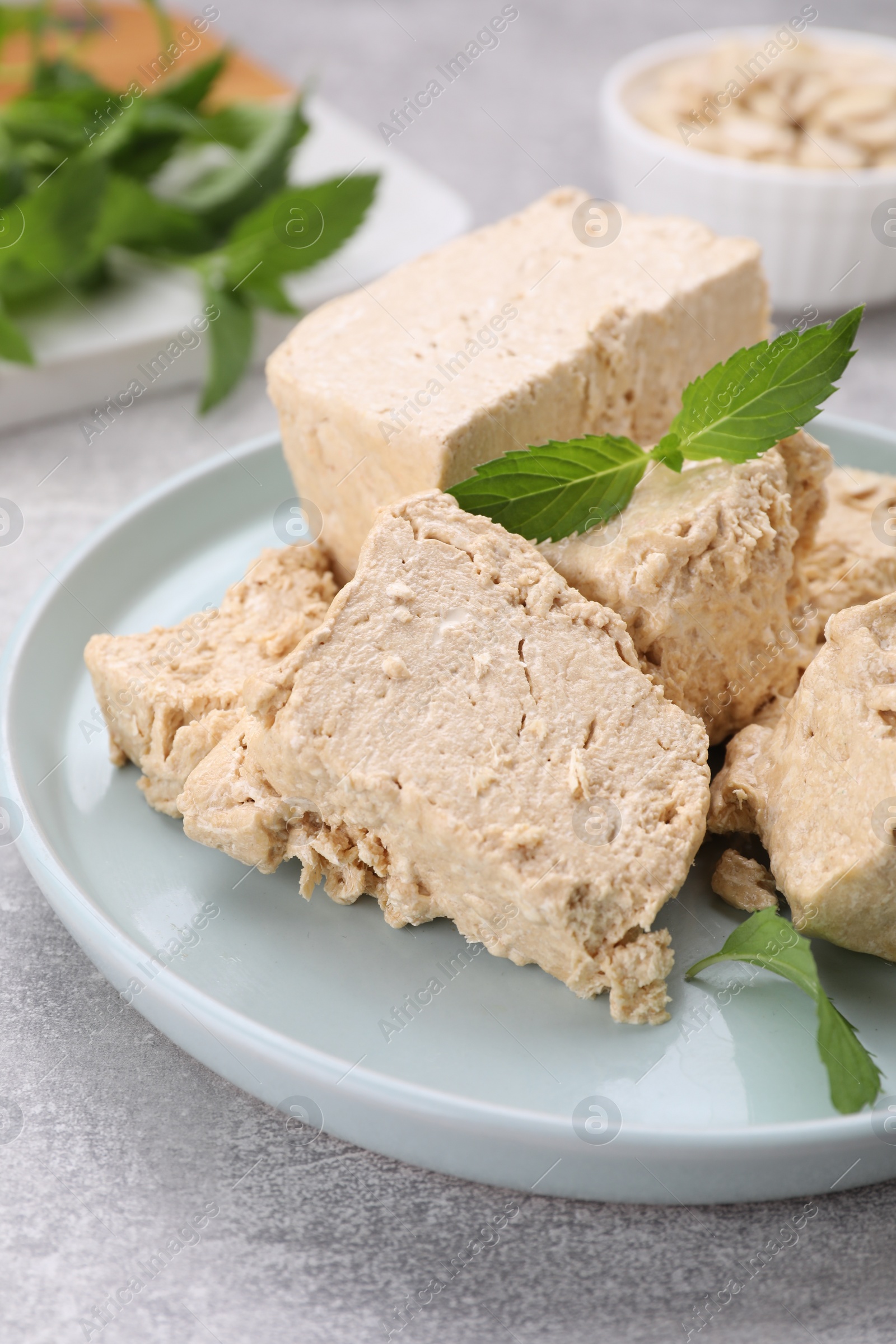 Photo of Plate with pieces of tasty halva and mint leaves on light grey table, closeup