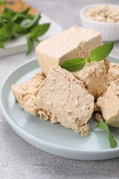 Plate with pieces of tasty halva and mint leaves on light grey table, closeup