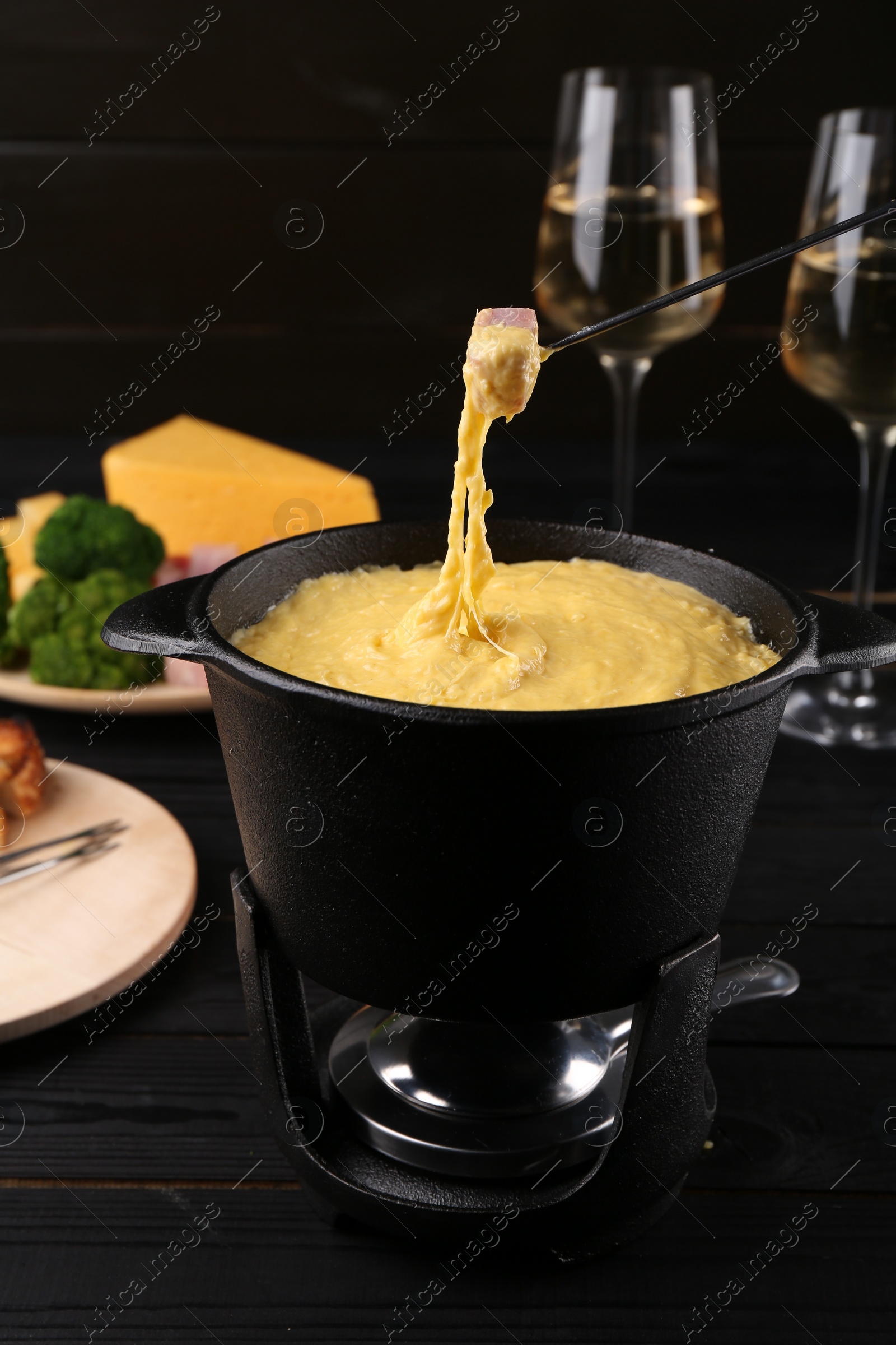 Photo of Dipping piece of ham into fondue pot with melted cheese on table