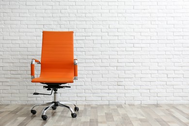 Comfortable office chair near white brick wall indoors. Space for text