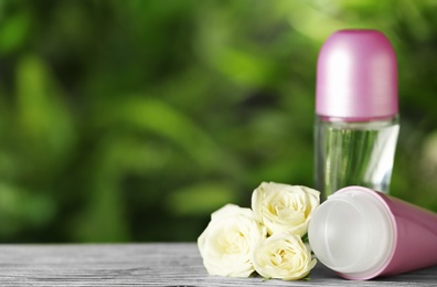 Photo of Natural deodorants with white roses on wooden table against blurred green background. Space for text