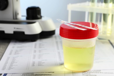 Photo of Container with urine sample for analysis on test forms in laboratory, closeup