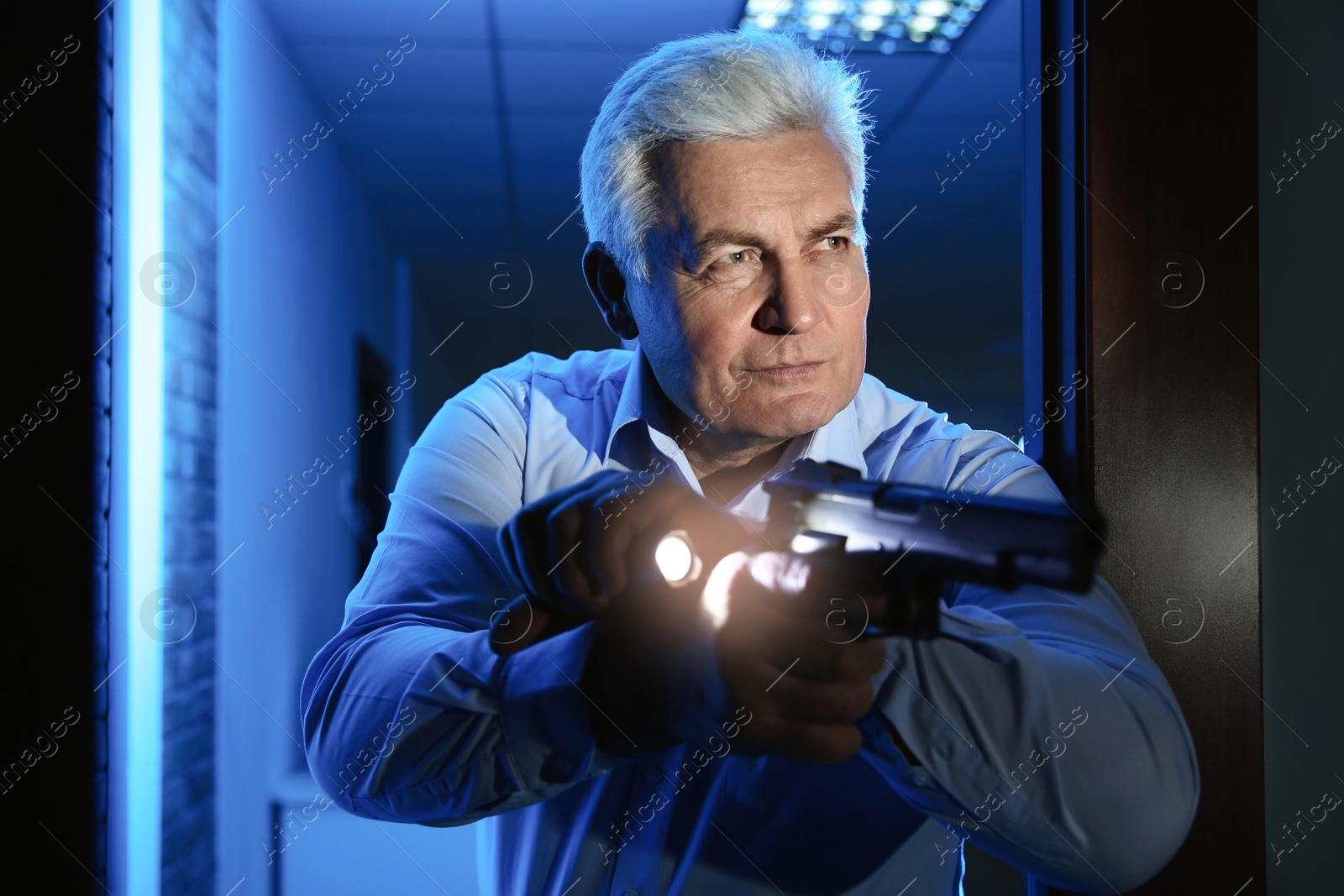 Photo of Professional security guard with gun and flashlight checking dark room