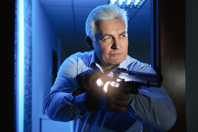 Professional security guard with gun and flashlight checking dark room