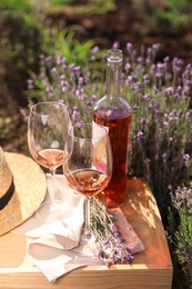 Bottle and glasses of wine on wooden table in lavender field