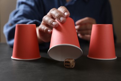 Photo of Woman playing thimblerig game with red cups and dice at black table, closeup