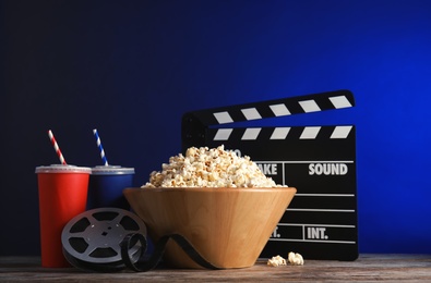 Photo of Composition with popcorn, cinema clapperboard and film reel on table against color background