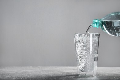 Photo of Pouring soda water from bottle into glass on grey table. Space for text
