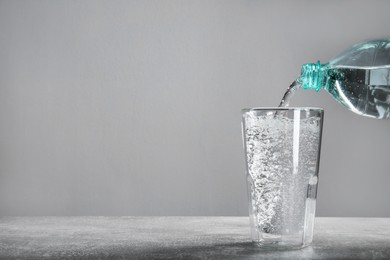 Pouring soda water from bottle into glass on grey table. Space for text