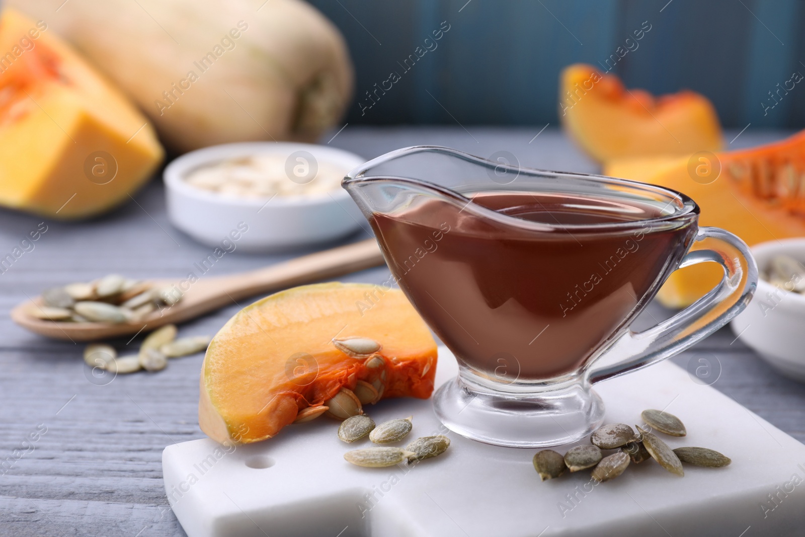 Photo of Fresh pumpkin seed oil in glass sauceboat on grey wooden table