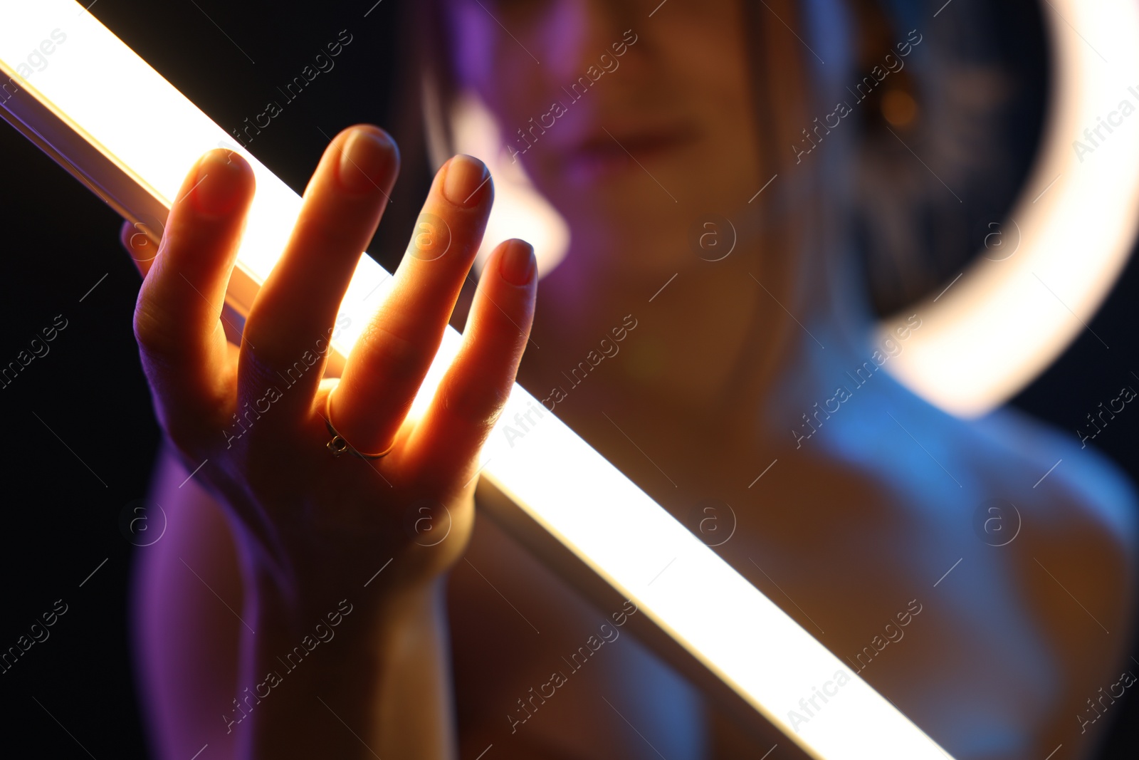 Photo of Woman with lamp on dark background in neon lights, closeup