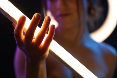 Photo of Woman with lamp on dark background in neon lights, closeup