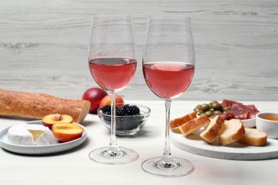 Photo of Glasses of delicious rose wine and snacks on white wooden table