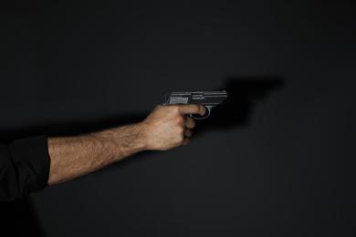 Photo of Professional killer with gun on black background, closeup