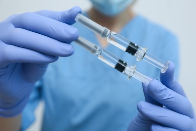 Photo of Doctor holding syringes with COVID-19 vaccine on light background, closeup