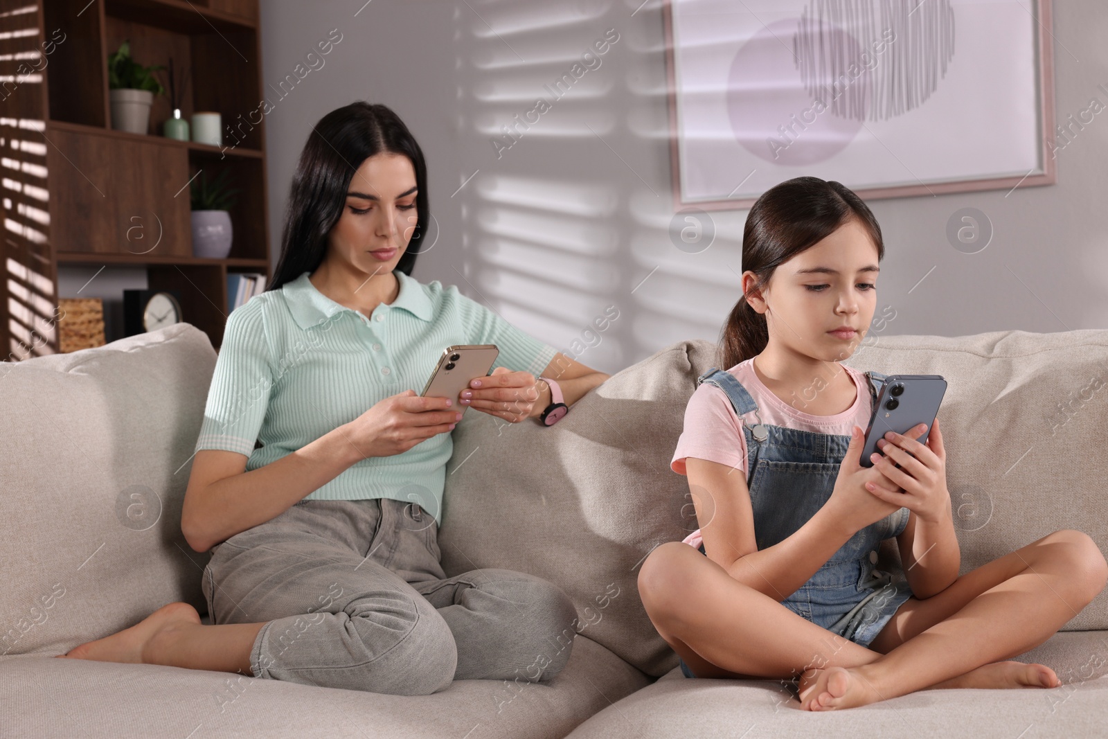 Photo of Internet addiction. Mother and her daughter with smartphones on sofa in living room