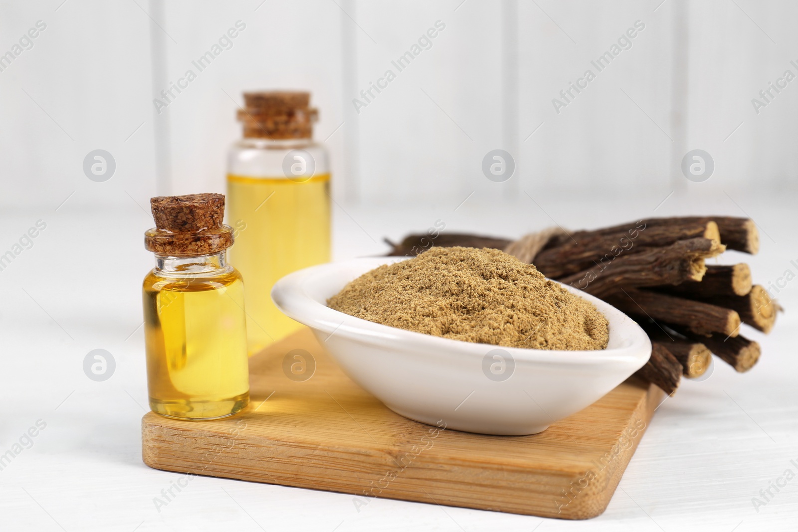 Photo of Dried sticks of licorice roots, bottles with essential oil and powder on white wooden table