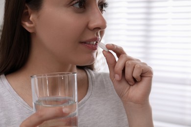 Photo of Young woman taking pill indoors, closeup view