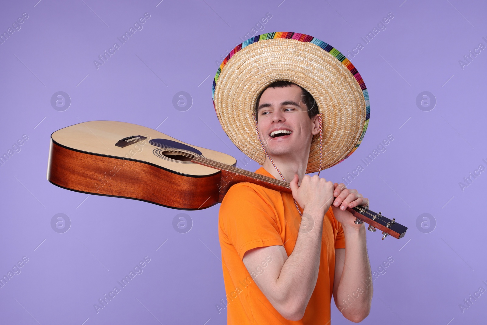 Photo of Young man in Mexican sombrero hat with guitar on violet background