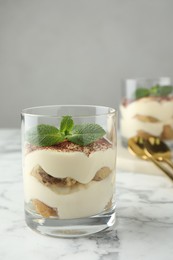 Photo of Delicious tiramisu in glass and mint leaves on white marble table