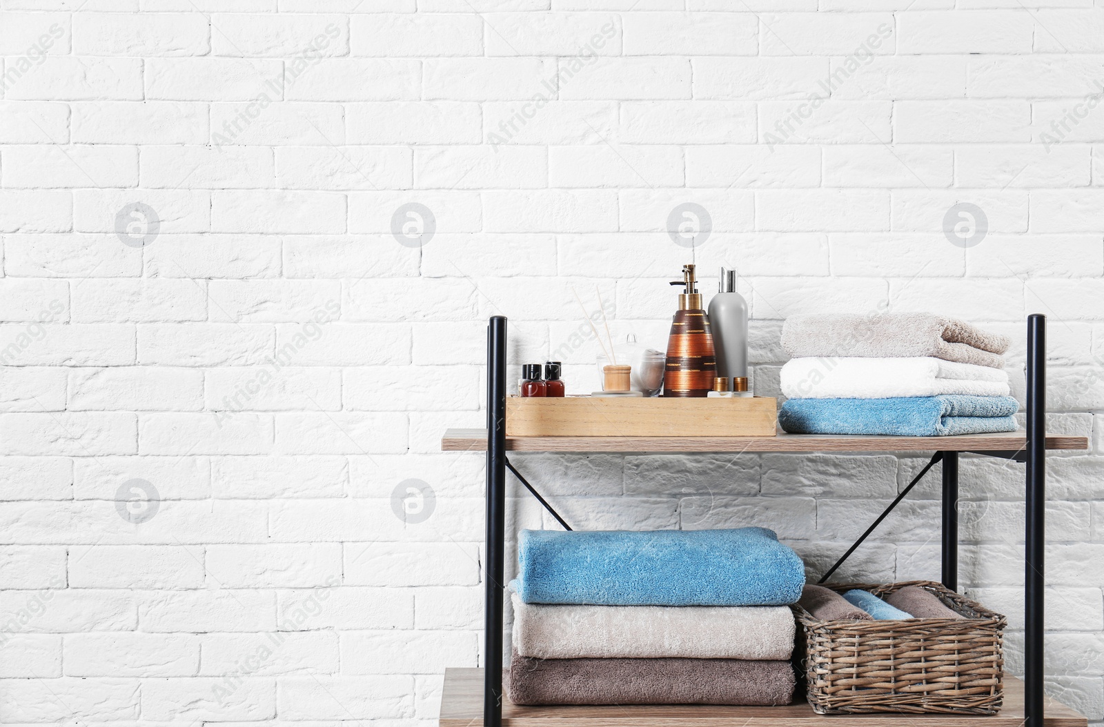 Photo of Shelving unit with clean towels and toiletries near brick wall. Space for text