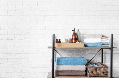 Shelving unit with clean towels and toiletries near brick wall. Space for text