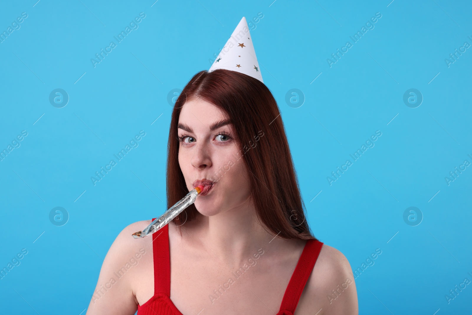 Photo of Young woman in party hat with blower on light blue background