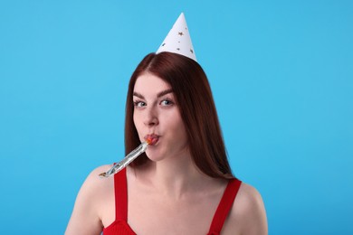 Young woman in party hat with blower on light blue background