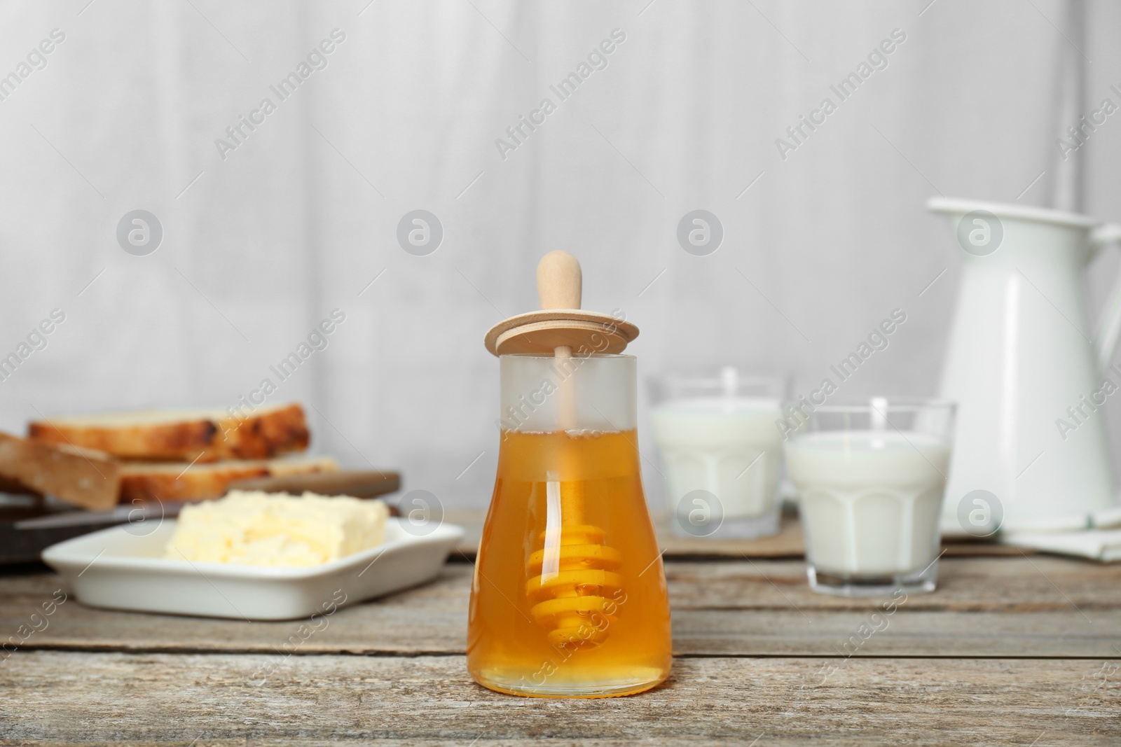 Photo of Jar of tasty honey, milk, butter and bread on wooden table