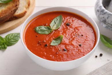 Photo of Delicious tomato cream soup in bowl on white wooden table, closeup